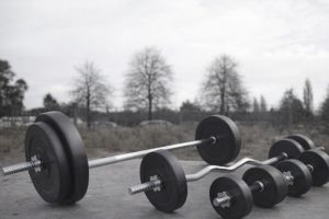 Tre skivstänger och hantlar med viktskivor ligger på marken utomhus.